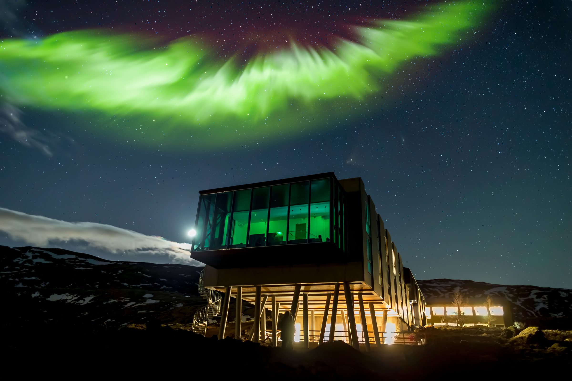 Norðurljós yfir upplýstu hóteli í íslenskri náttúru